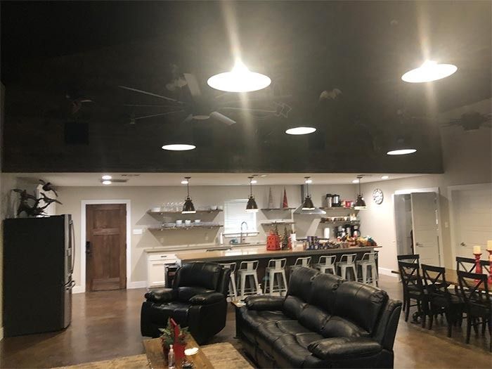 A spacious room with a kitchen island, black leather seating, and a large black ceiling with pendant lighting.