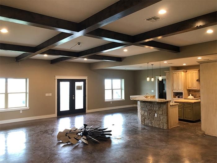 A wide-open room featuring stained concrete floors, dark ceiling beams, and a stone-accented kitchen island.
