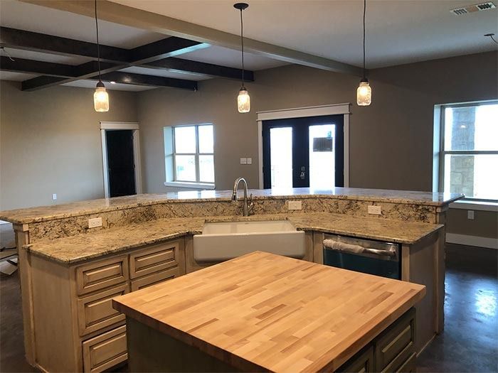 Kitchen with an island featuring a wooden countertop, a farmhouse sink, granite countertops, and dark wood ceiling beams.