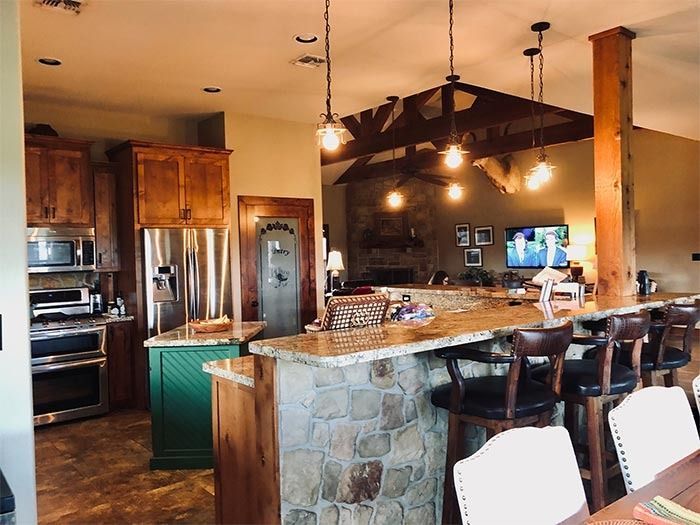 A rustic-style kitchen and breakfast bar with wood cabinets, stone siding, overhead pendant lights, and bar stools.