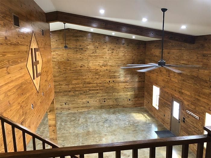 High-angle view of a rustic, vaulted room with wood-paneled walls, a concrete floor, and a large ceiling fan.