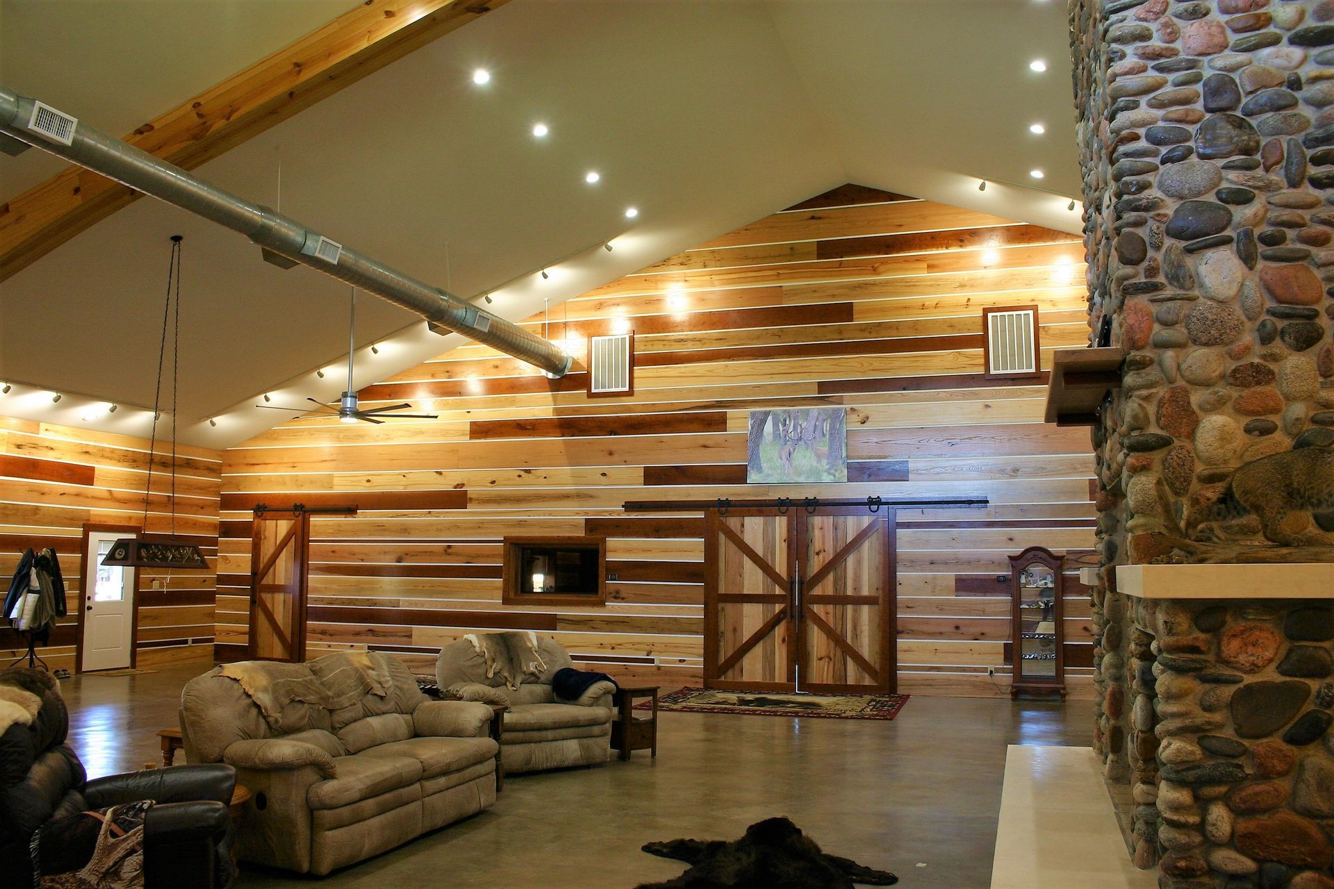 A spacious room with a high vaulted ceiling, horizontal wood-paneled walls, a large stone fireplace, and rustic furniture.