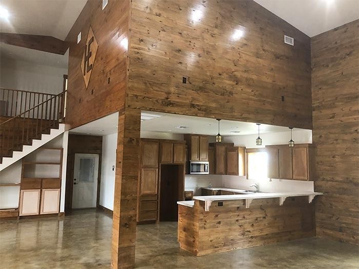 An open-concept rustic room featuring wooden wall paneling, concrete floors, a kitchen area, and a staircase.