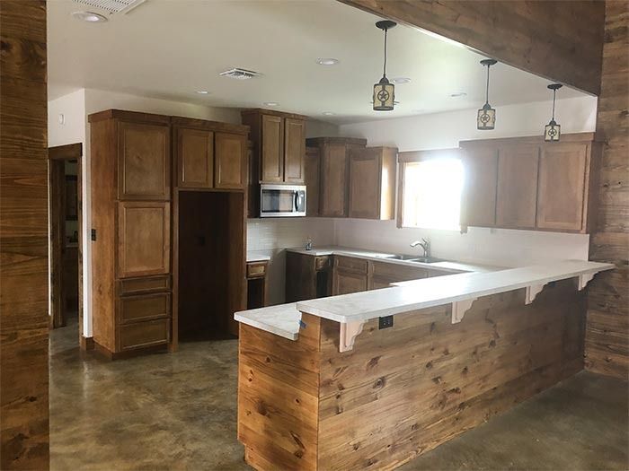 A kitchen with wooden cabinets, a light-colored countertop, an island, and pendant lighting over a concrete floor.