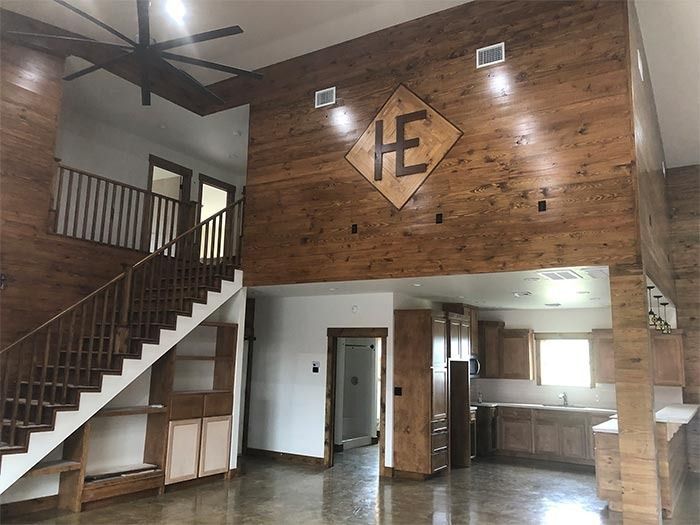 A two-story open-concept room with wood walls, a wooden staircase, a mezzanine, and a kitchen area.