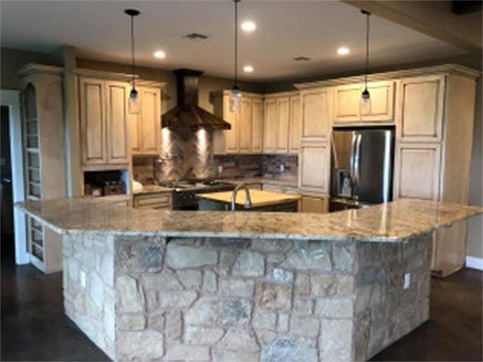 A kitchen features light wood cabinets, granite countertops, and a stone-fronted island, with a stainless steel refrigerator.