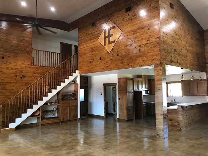 Rustic interior of a large, high-ceilinged lodge with wood-paneled walls, a staircase, and a kitchen area.