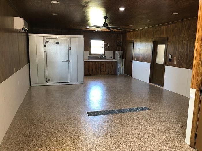 A spacious room with wood-paneled walls, a large metal walk-in cooler, a small kitchen counter, and a speckled floor.