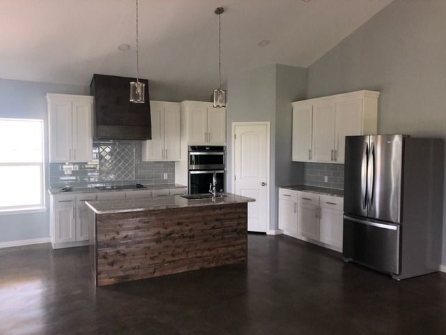 A kitchen featuring white cabinets, a dark wood-paneled island, stainless steel appliances, and a dark vent hood.