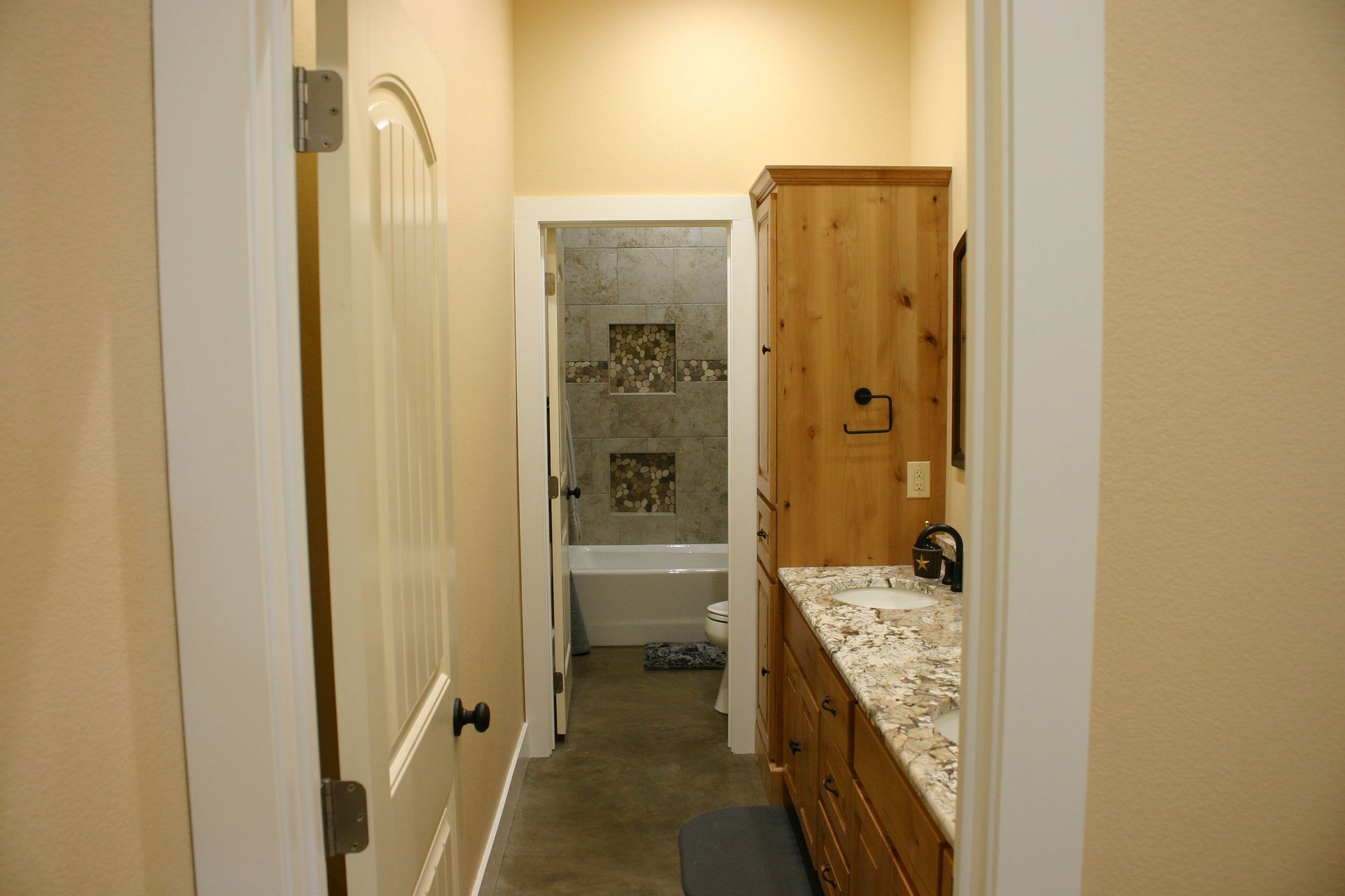 A view from a doorway into a bathroom with a wooden vanity, marble countertop, and a tiled shower/tub area in the rear.
