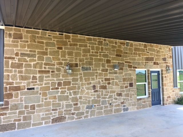 A tan and brown stone exterior wall with a blue door and window under a dark metal awning on a concrete patio.