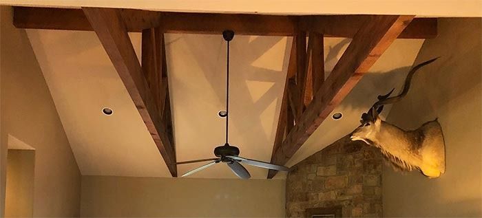 A ceiling fan hangs between two wooden beams in a high-vaulted room, with an antelope taxidermy mount on the wall.