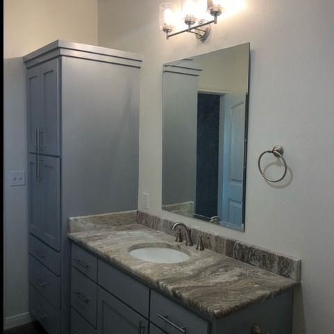Bathroom vanity with a grey cabinet tower and drawers, marble-patterned countertop, sink, mirror, and wall lighting.