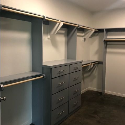 Walk-in closet with gray custom shelving, a central tower of eight drawers, and wooden hanging rods on a dark carpet.