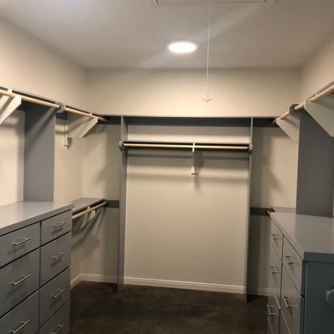 A walk-in closet featuring gray built-in dressers, white shelves, and wooden hanging rods on three walls.