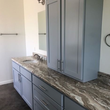 A bathroom vanity with gray cabinets, a marbled countertop, a sink, and a matching wall cabinet with a mirror.