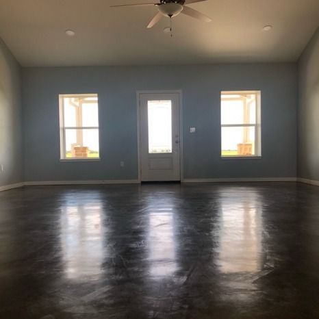 A view of a modern, empty room with light gray walls, high-gloss concrete floors, a ceiling fan, and three centered doors.