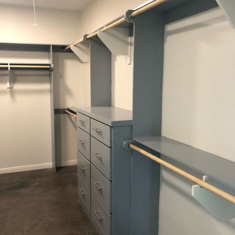 An empty walk-in closet with blue shelving, built-in drawers, and wooden hanging rods against white walls.