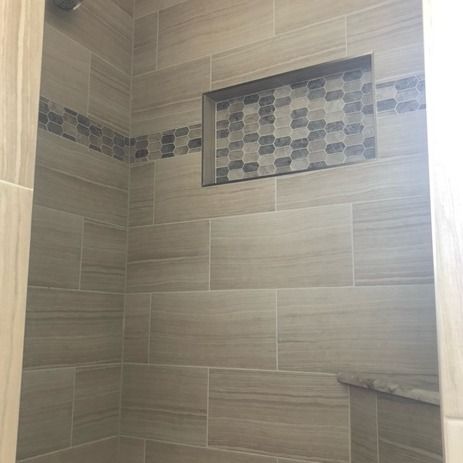 A shower wall tiled in horizontal beige stone, featuring a recessed niche with patterned, multi-colored mosaic tiles.