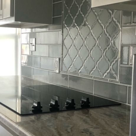 A close-up of a kitchen backsplash featuring gray subway tiles and a central decorative lantern-style tile pattern.