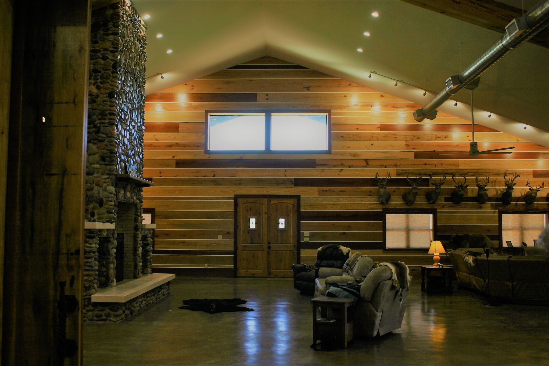 A large rustic living room with wood paneled walls, a stone fireplace, high vaulted ceilings, and comfortable seating.