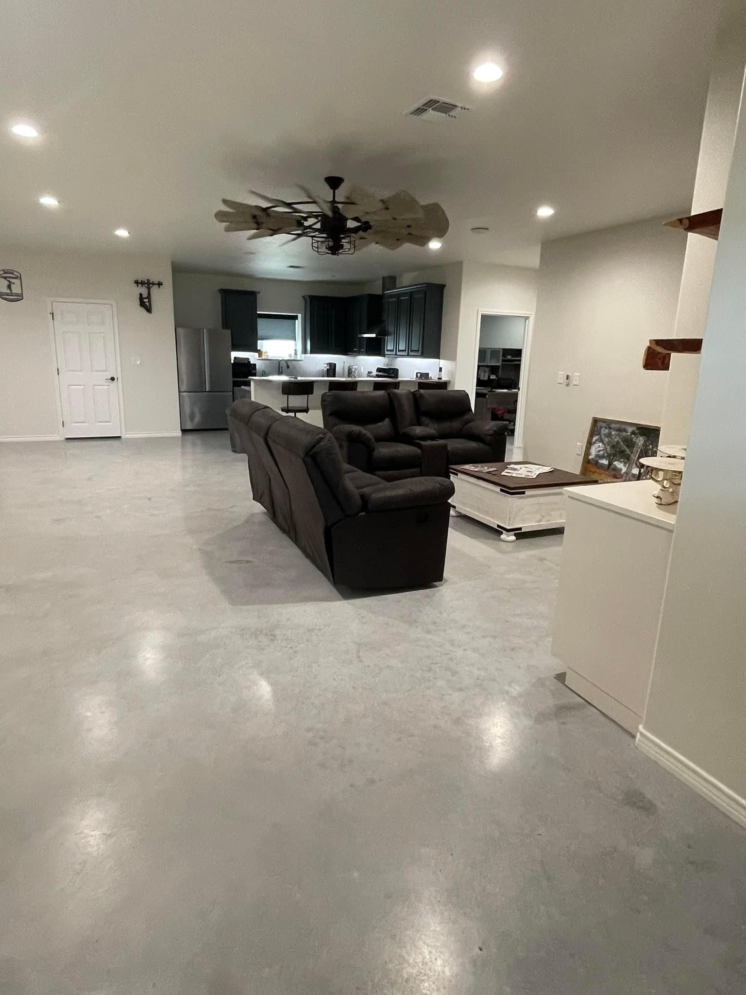 An open-concept living area with polished concrete floors, a dark gray sofa, a coffee table, and a kitchen in the back.