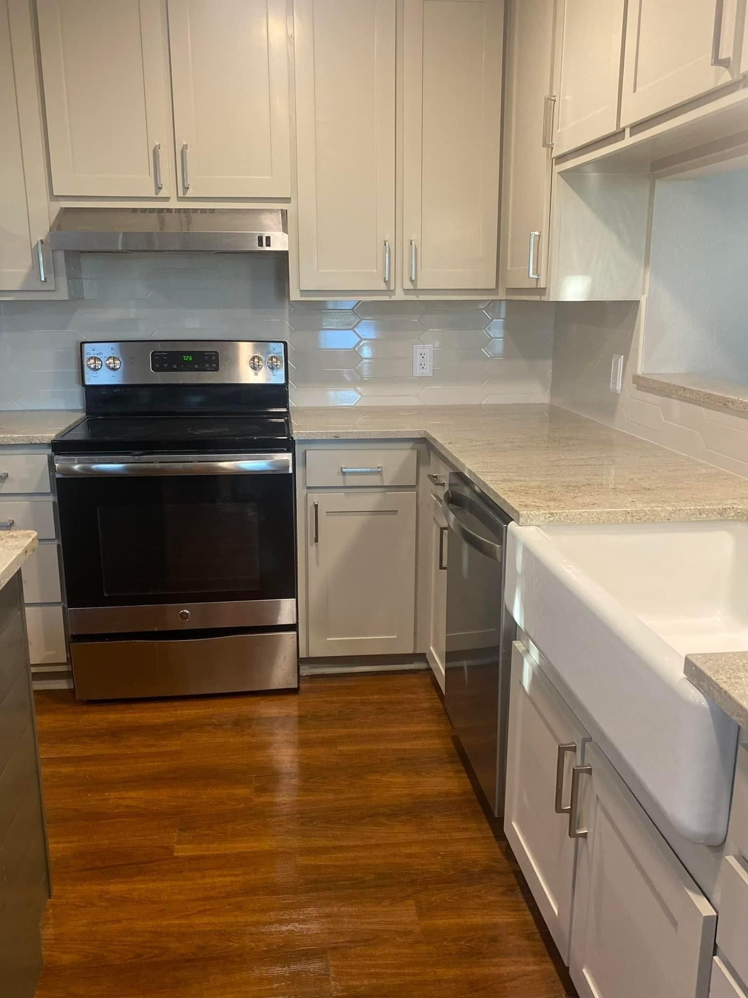 Modern kitchen with white shaker cabinets, light granite countertops, a stainless steel stove, and a white farmhouse sink.