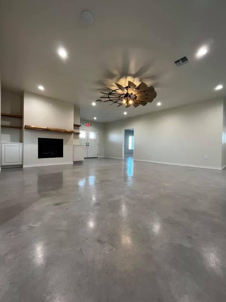 A spacious, modern room with polished concrete floors, recessed lighting, a fireplace with a wood mantel, and a fan.