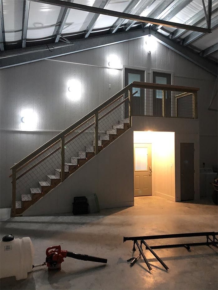 Staircase with wooden railings leading to a loft above a ground-level doorway in a spacious, light-filled garage.