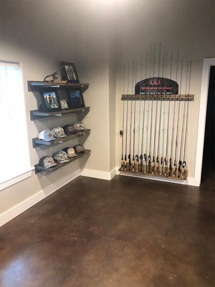 A room with wood-toned concrete floors featuring three wall-mounted shelves displaying hats and a wall-mounted rod rack.