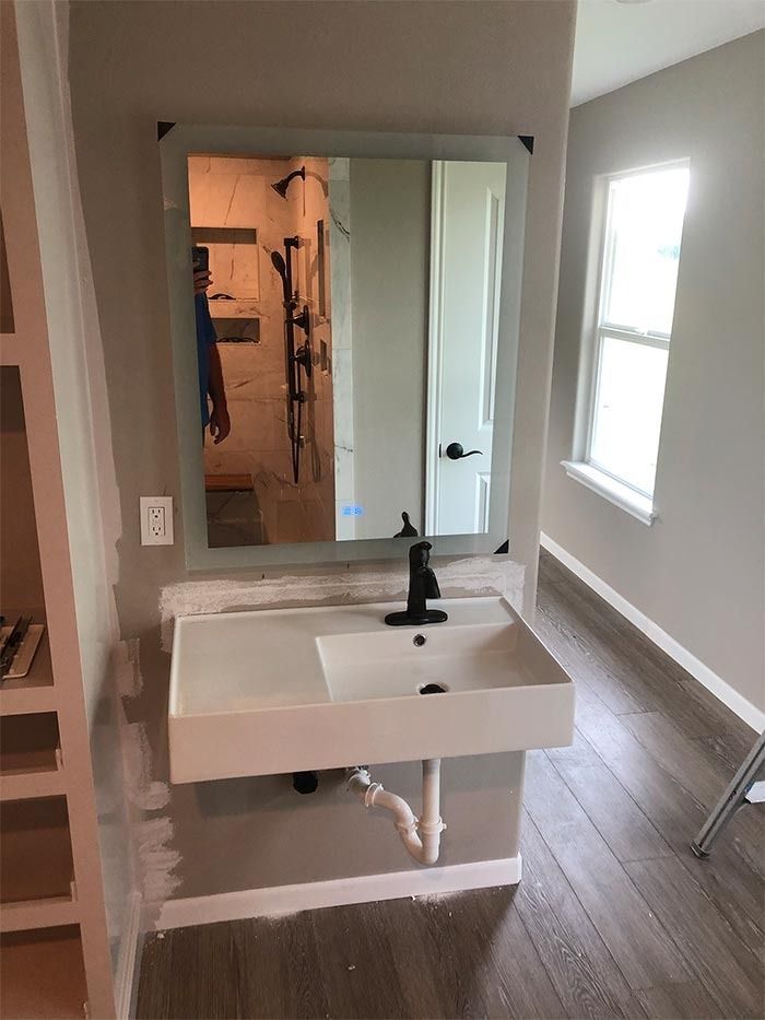 A wall-mounted white vanity with a black faucet, mirror, and exposed plumbing in a bathroom with wood-look flooring.