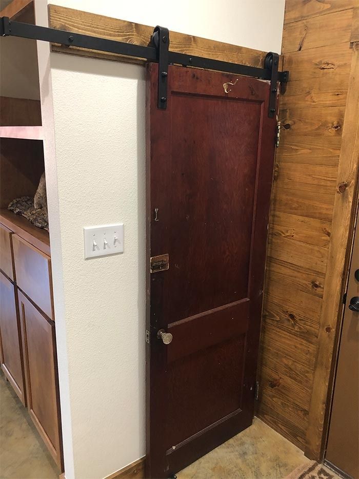 A dark wood sliding barn door mounted on a black metal rail in a room with white walls and wood paneling.