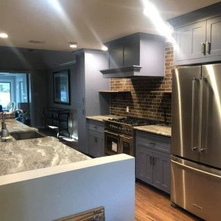 A modern kitchen with blue-grey cabinets, a stainless steel refrigerator, and a brick backsplash over a gas stove.