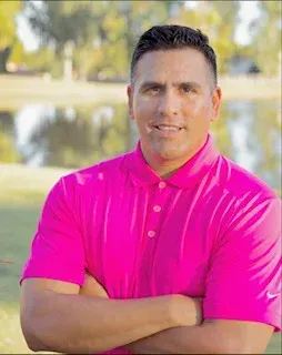 A man in a pink shirt is standing with his arms crossed.