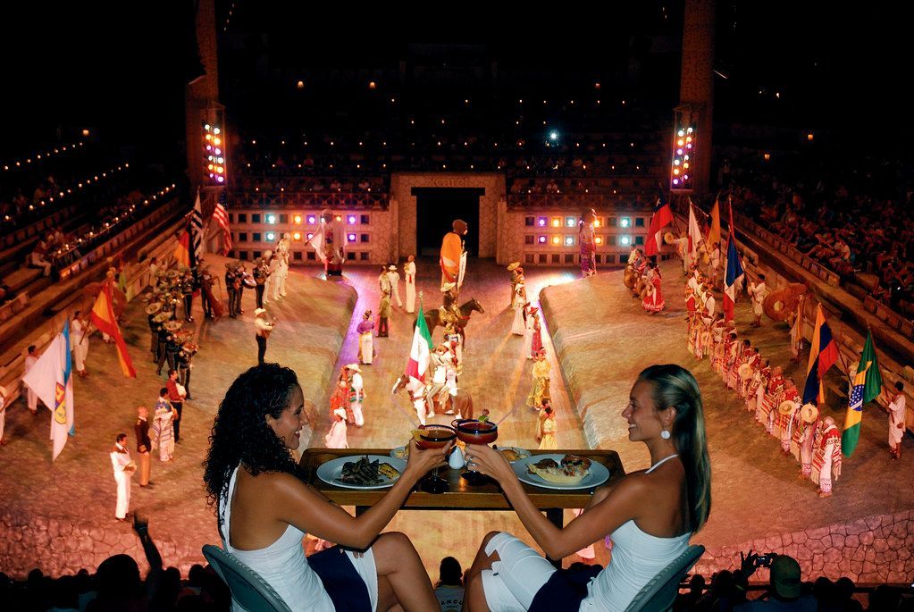 Two women are sitting at a table in front of a crowd watching a show in Cancun