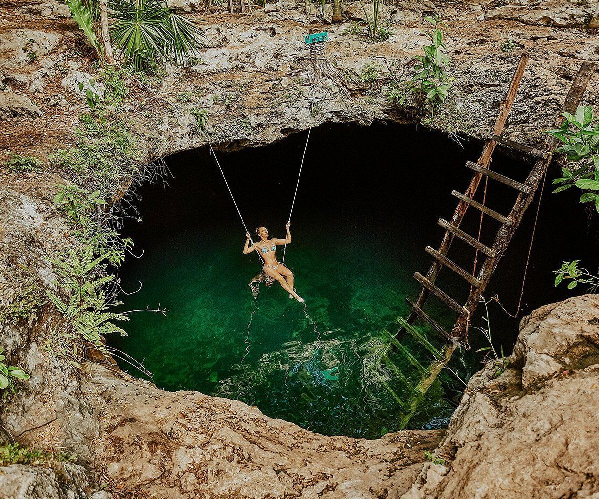 A person is hanging from a swing in a hole in the water.
