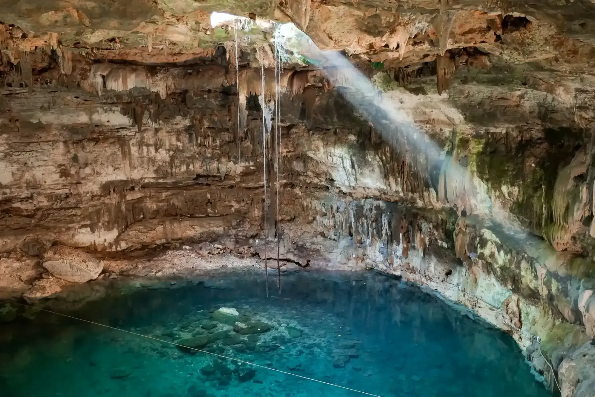 The sun is shining through the ceiling of a cave into a pool of water.