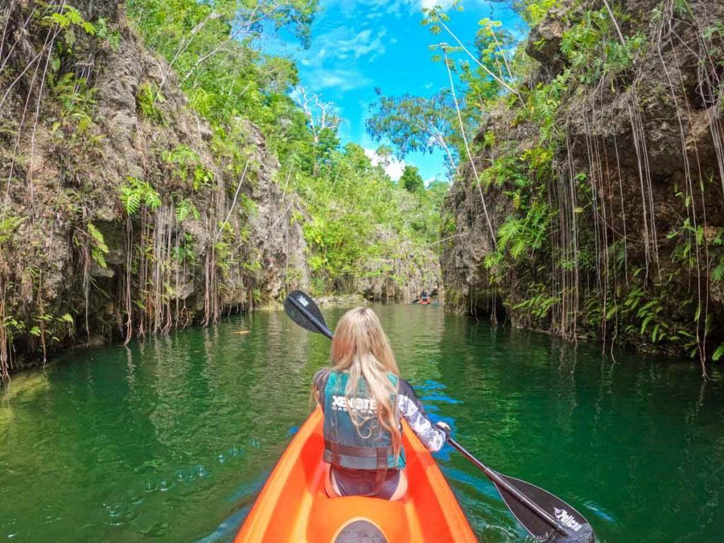 A woman is paddling an orange kayak down a river.