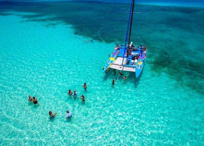 A group of people are swimming in the ocean near a sailboat.