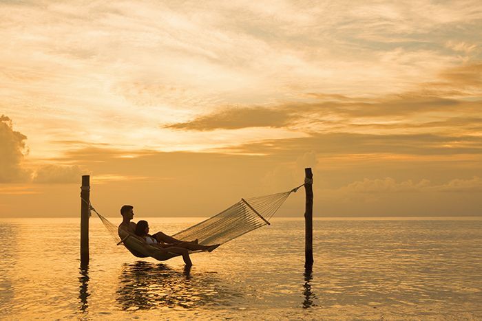 Una pareja relajándose viendo el atardecer en la playa sobre una hamaca.