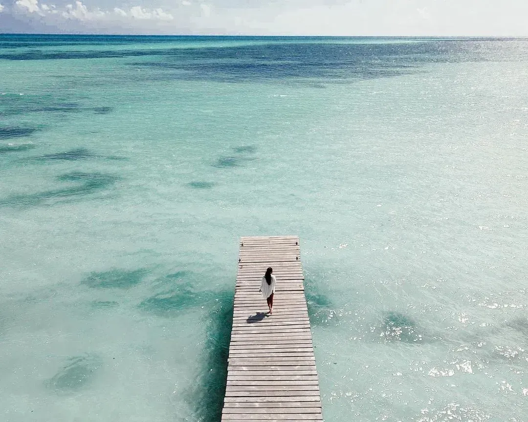 Una persona caminando sobre un muelle rodeada de mar.