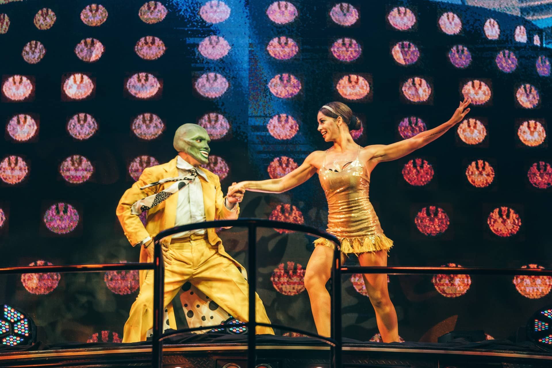 A man in a yellow suit and a woman in a gold dress are dancing on a stage.