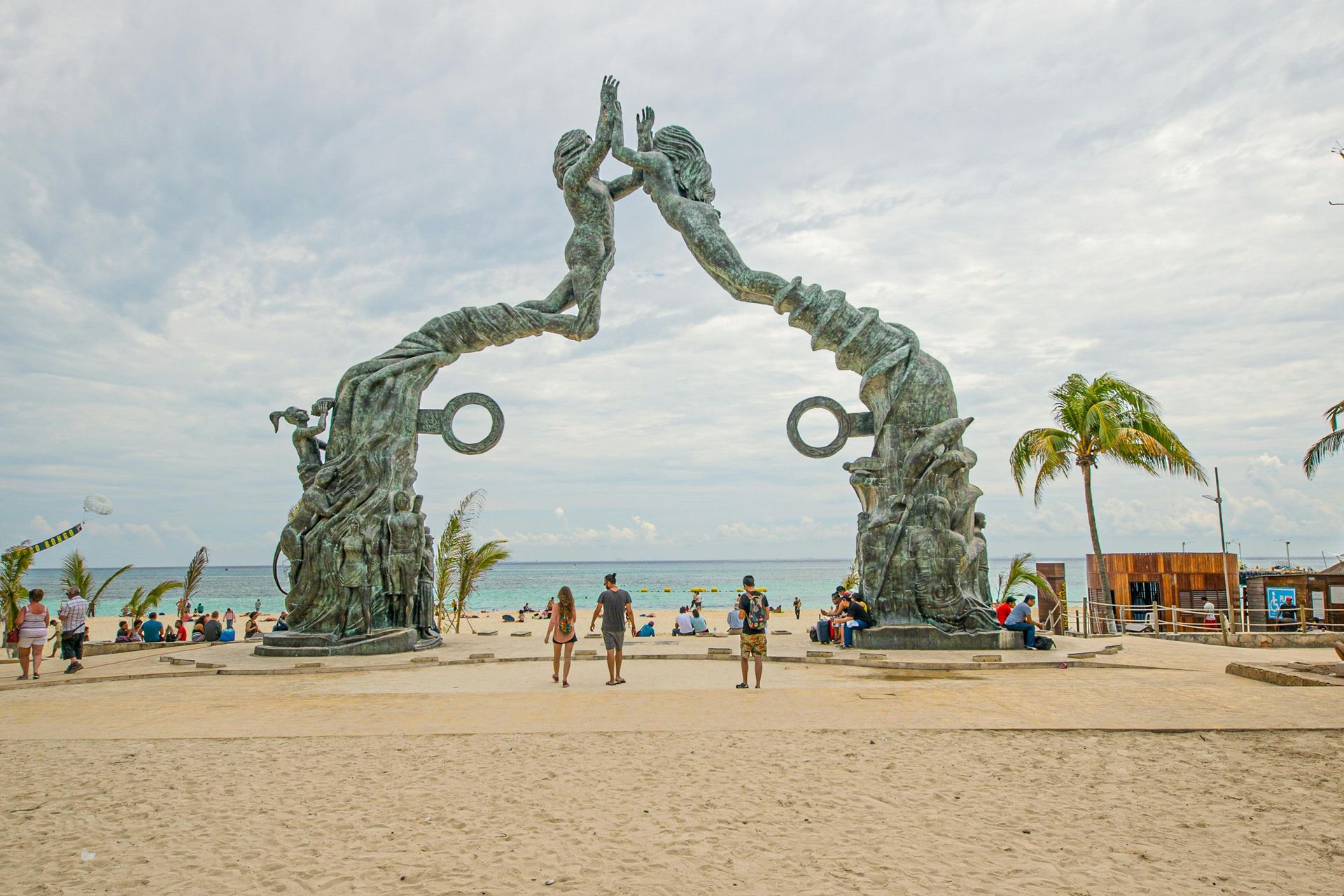 A group of people are standing in front of a statue on a beach.