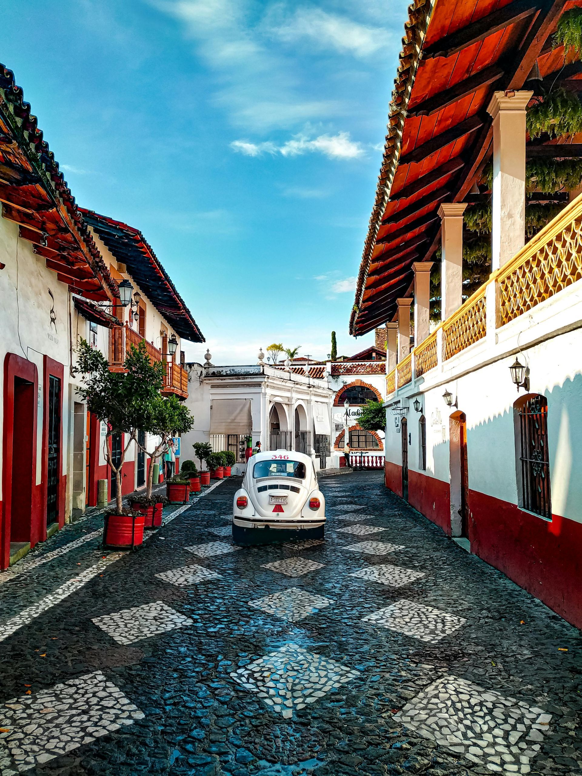 A white car is driving down a cobblestone street between two buildings.