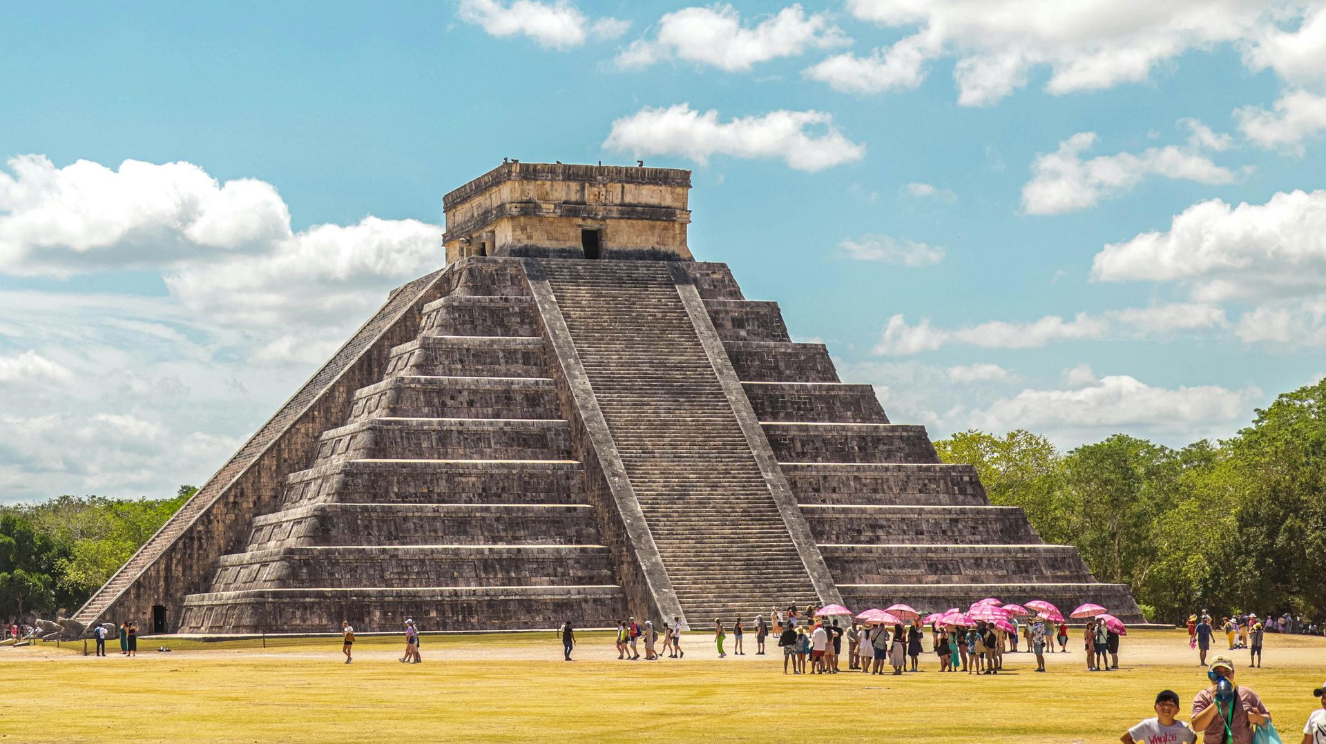 A group of people are standing in front of a large stone pyramid.