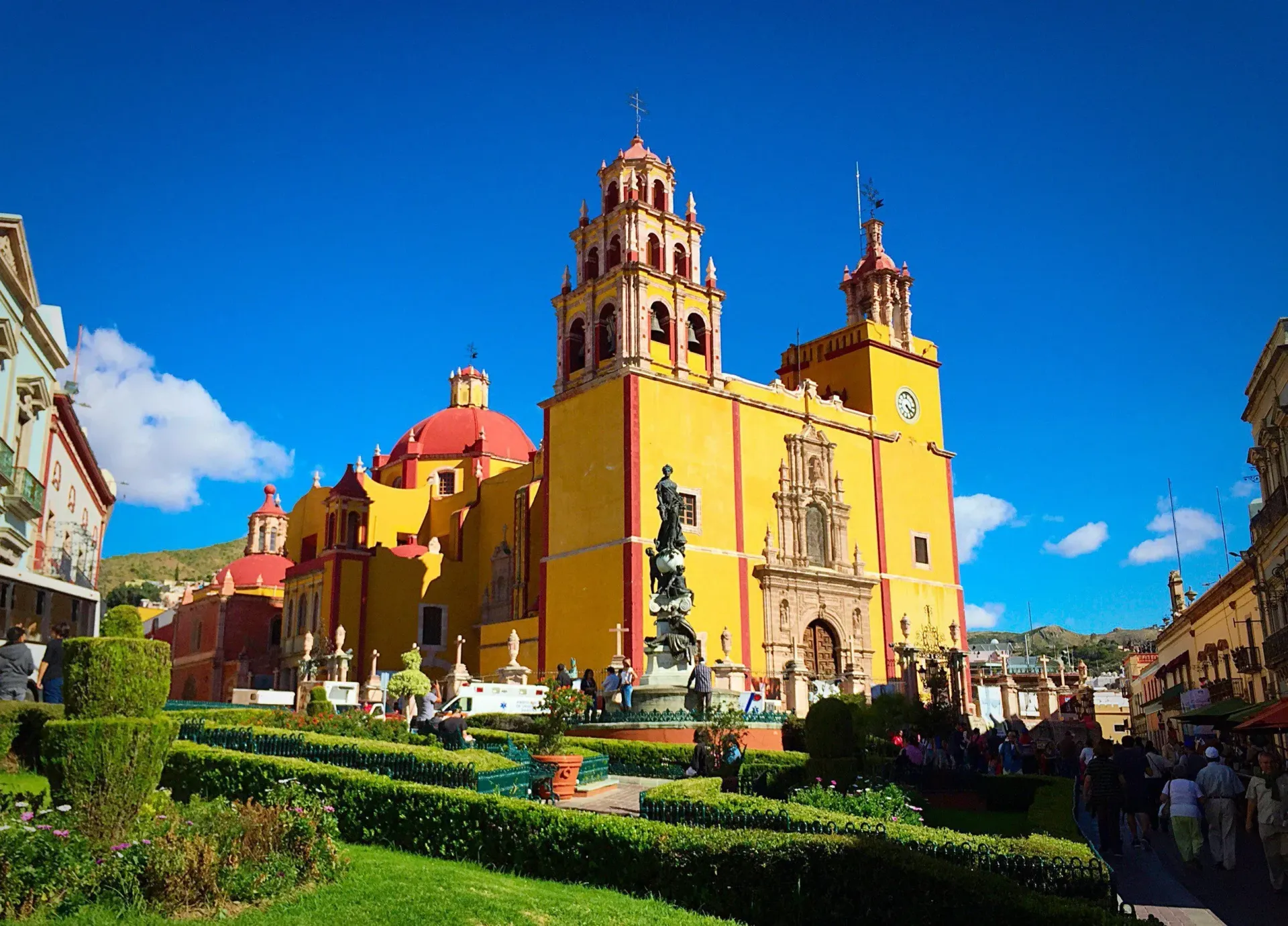 A large yellow and red church with a clock tower in a park.