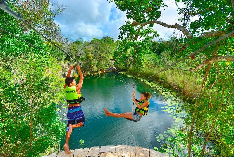 A man and a woman are riding a zip line over a lake.
