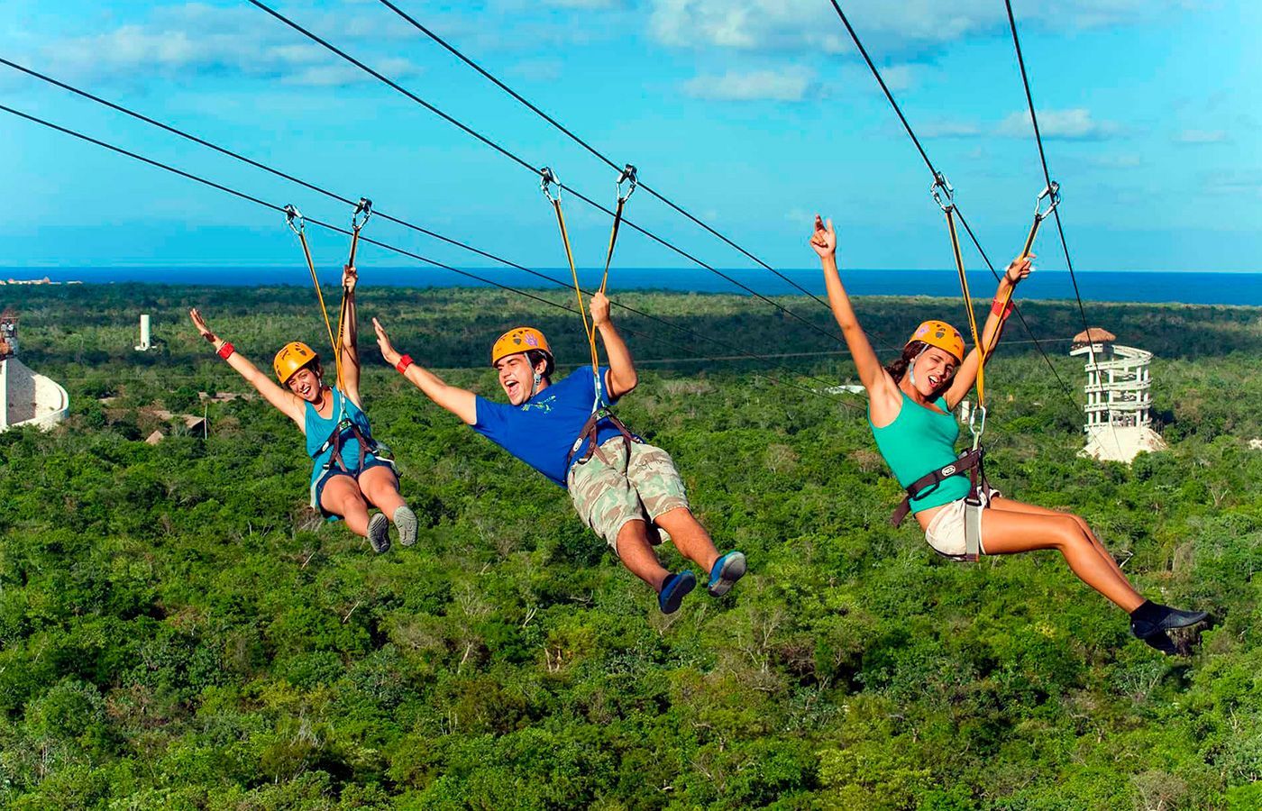 Three people are riding a zip line over a grassy field.