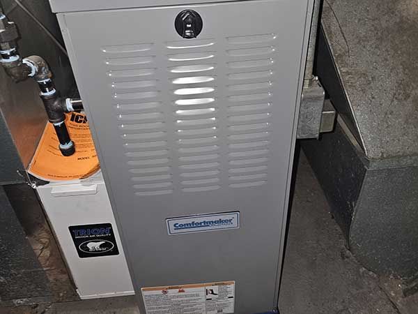 A gas furnace is sitting in a basement next to a water heater.