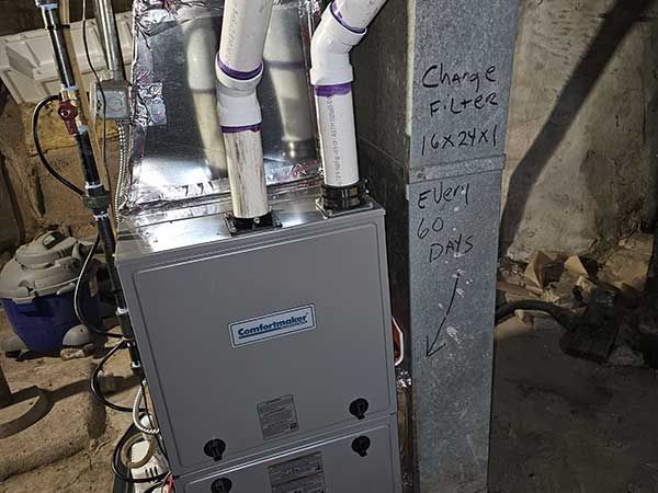 A furnace is sitting in a basement next to a pipe.